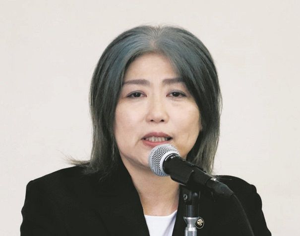 田久保真紀が黒い服を着てマイクに向かって喋っている。
