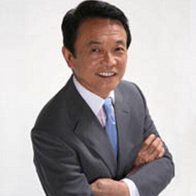 濃い灰色のスーツに水色のネクタイを着用し、腕を組んで微笑んでいる麻生太郎氏の肖像写真です。