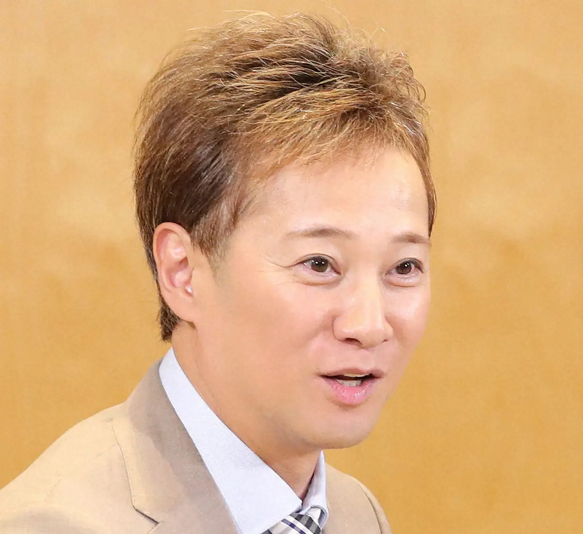 中居正広さんの上半身アップのポートレート。笑顔で、ベージュのスーツを着ている。