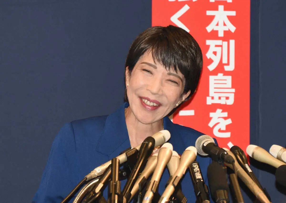 高市早苗さんが多数のマイクの前で笑顔で話している様子。記者会見の場面を捉えている。