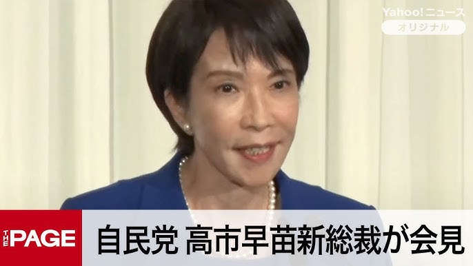 ブルーのジャケットとパールのネックレスを着用し、会見で話す高市早苗氏。政治家としての公的な権威性を示すニュース映像。