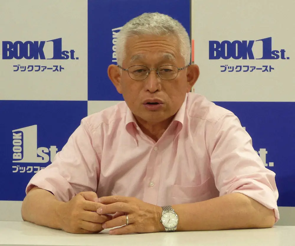 ピンクのシャツを着て、ブックファーストのロゴを背景にイベントで話す田崎史郎さん。