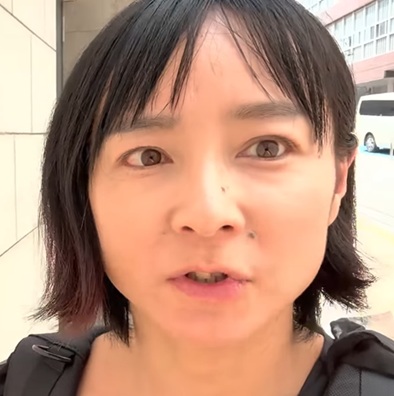 屋外でカメラに向かって話している短い黒髪の日本の女性の顔のアップ。