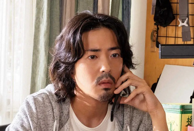 スマートフォンで深刻な表情をして通話する、髭をたくわえた若葉竜也