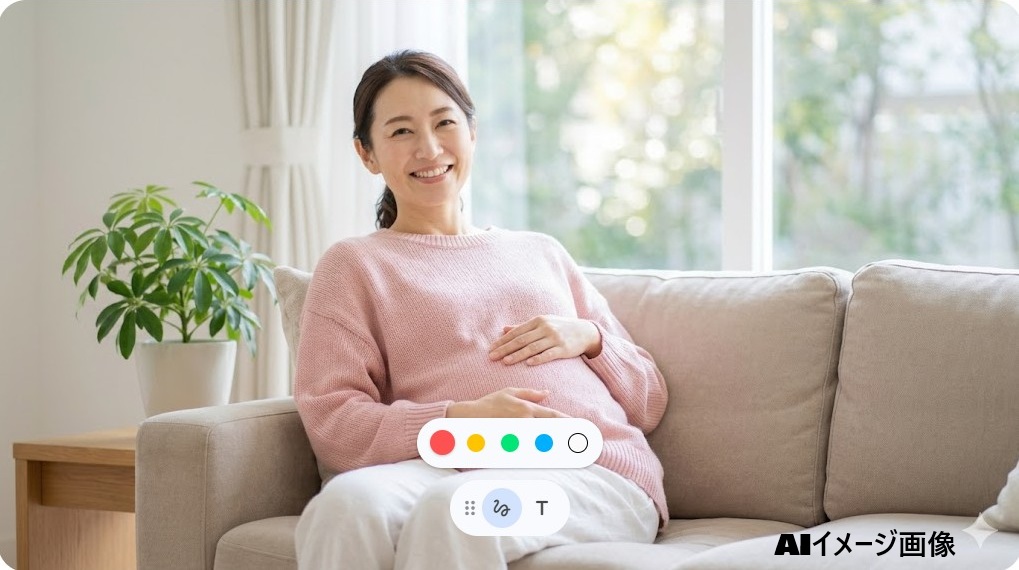 笑顔でお腹に手を添えてソファに座る妊娠中の日本人女性